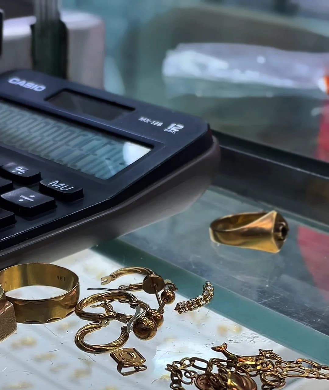 Anillos, argollas y cadenas de oro en desuso junto a la calculadora en el mostrador